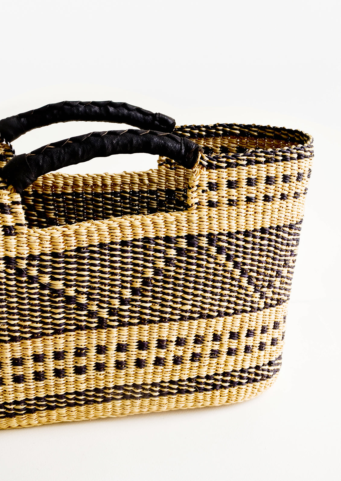 Black leather cutout handles on woven elephant grass tote