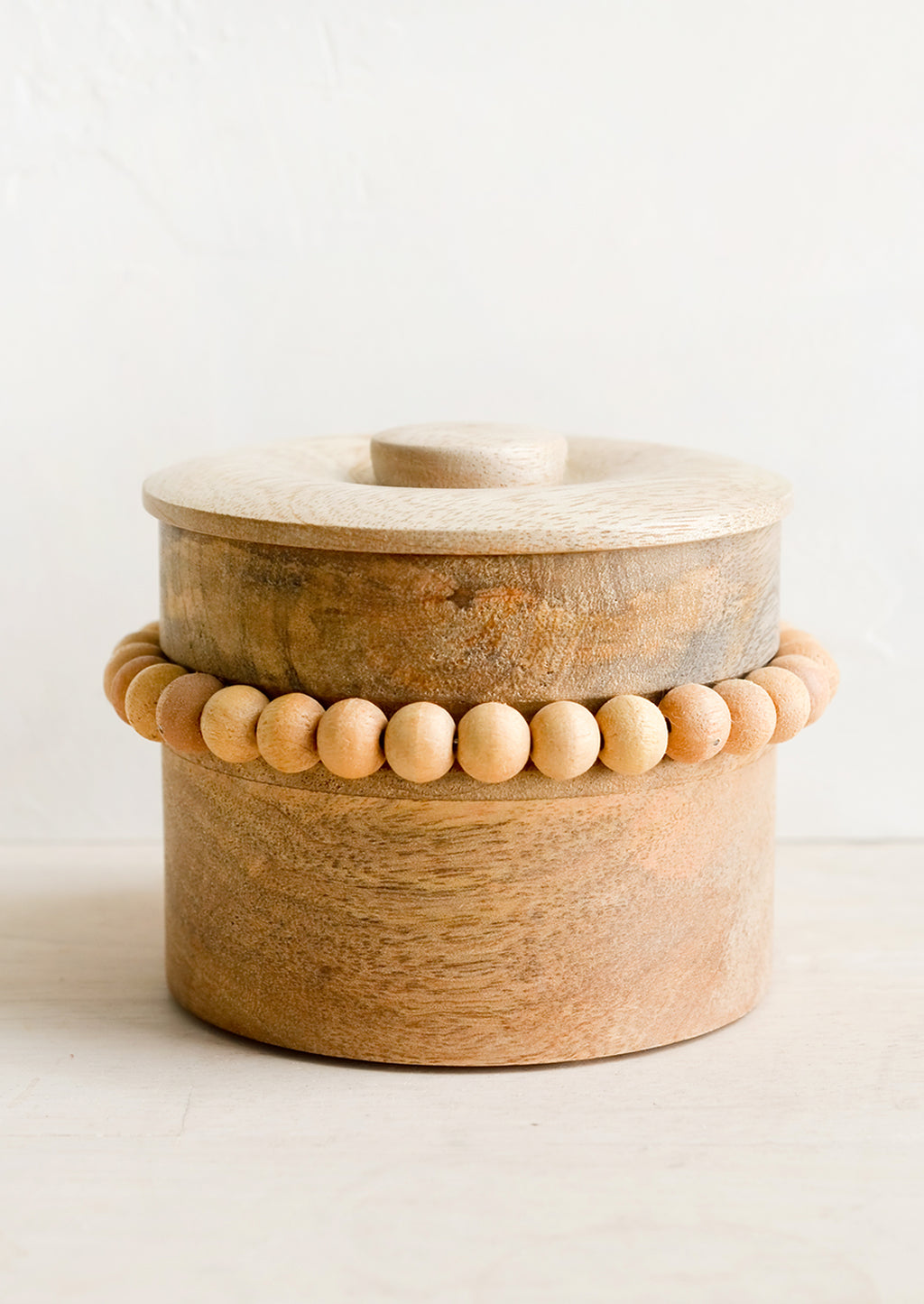 1: A round wooden storage box with lid and wooden beaded detailing.