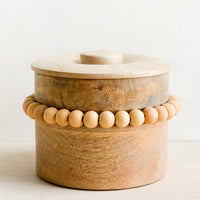 1: A round wooden storage box with lid and wooden beaded detailing.