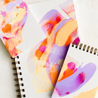 1: Vibrantly painted white notebooks with purple, pink and orange paint.