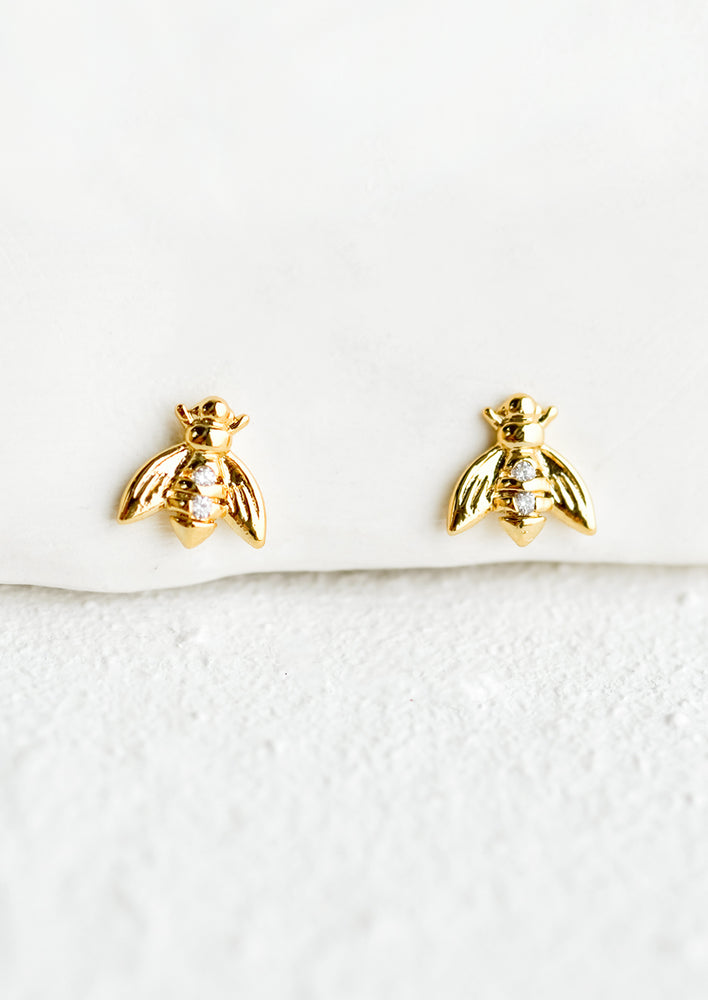 1: A pair of small gold stud earrings in the shape of bees with crystal detailing at middle.