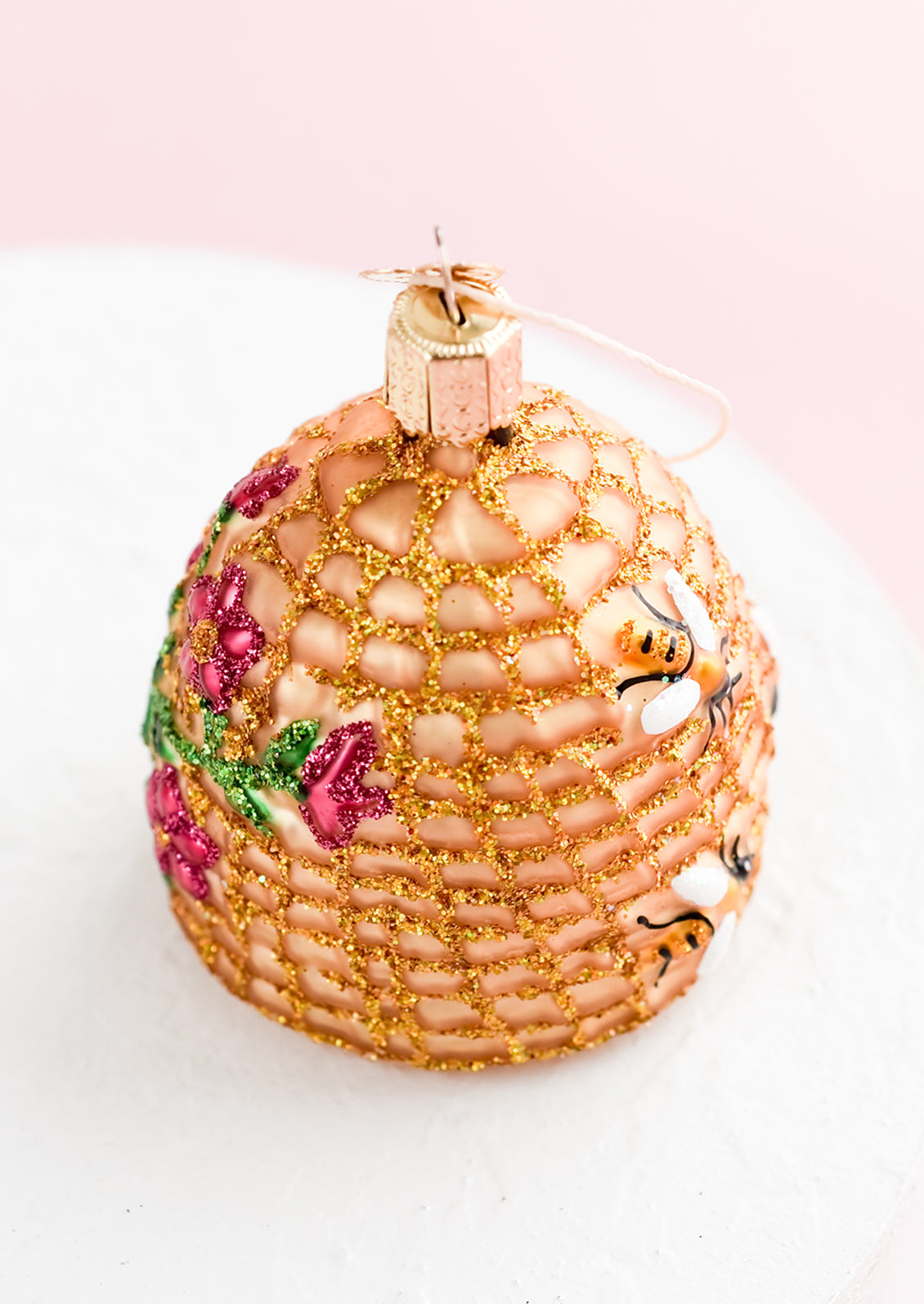A glass ornament in shape of beehive with pink flowers.