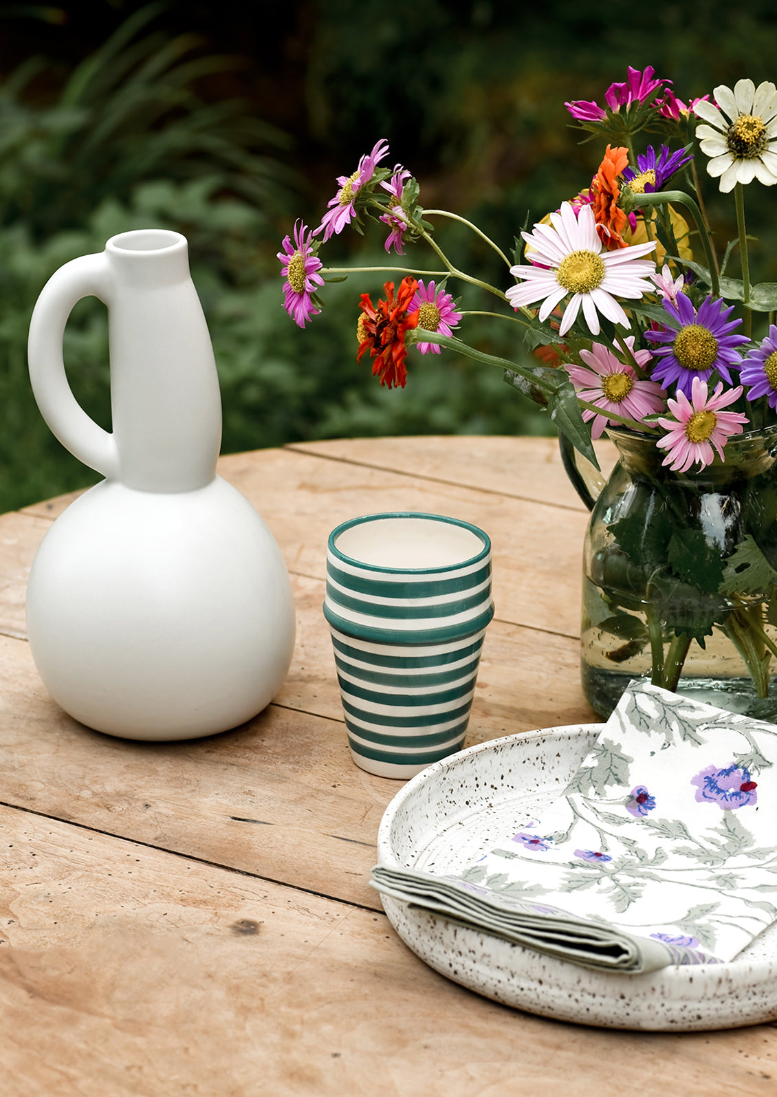 A table setting with pitcher, cup and flowers.