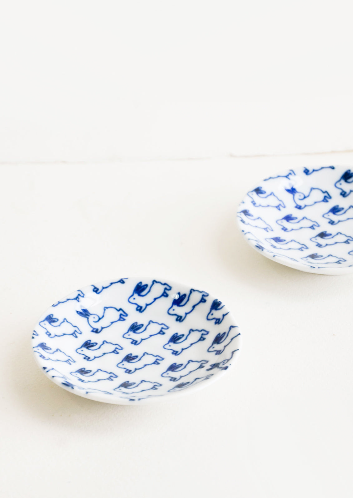 Small, round ceramic plate in white with allover bunny print in blue