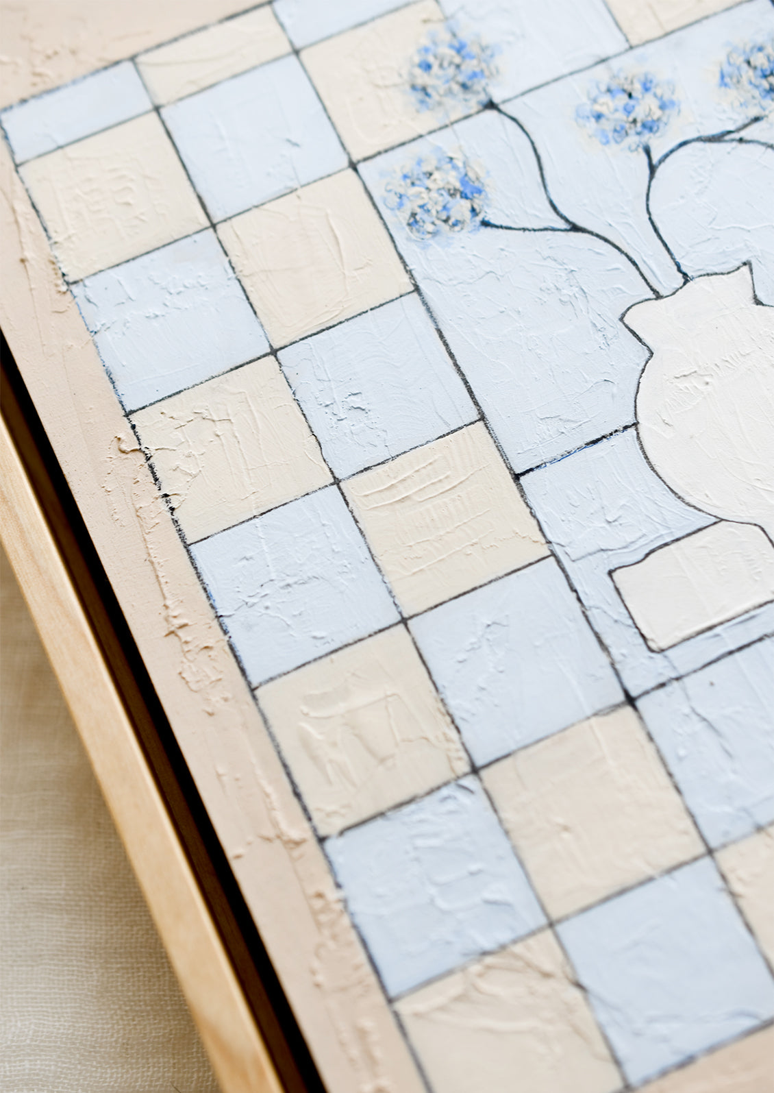 A framed original painting of still life vase with flowers on a checkered beige and periwinkle background.