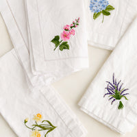 4: Four white cotton napkins with colorful botanical embroidery.