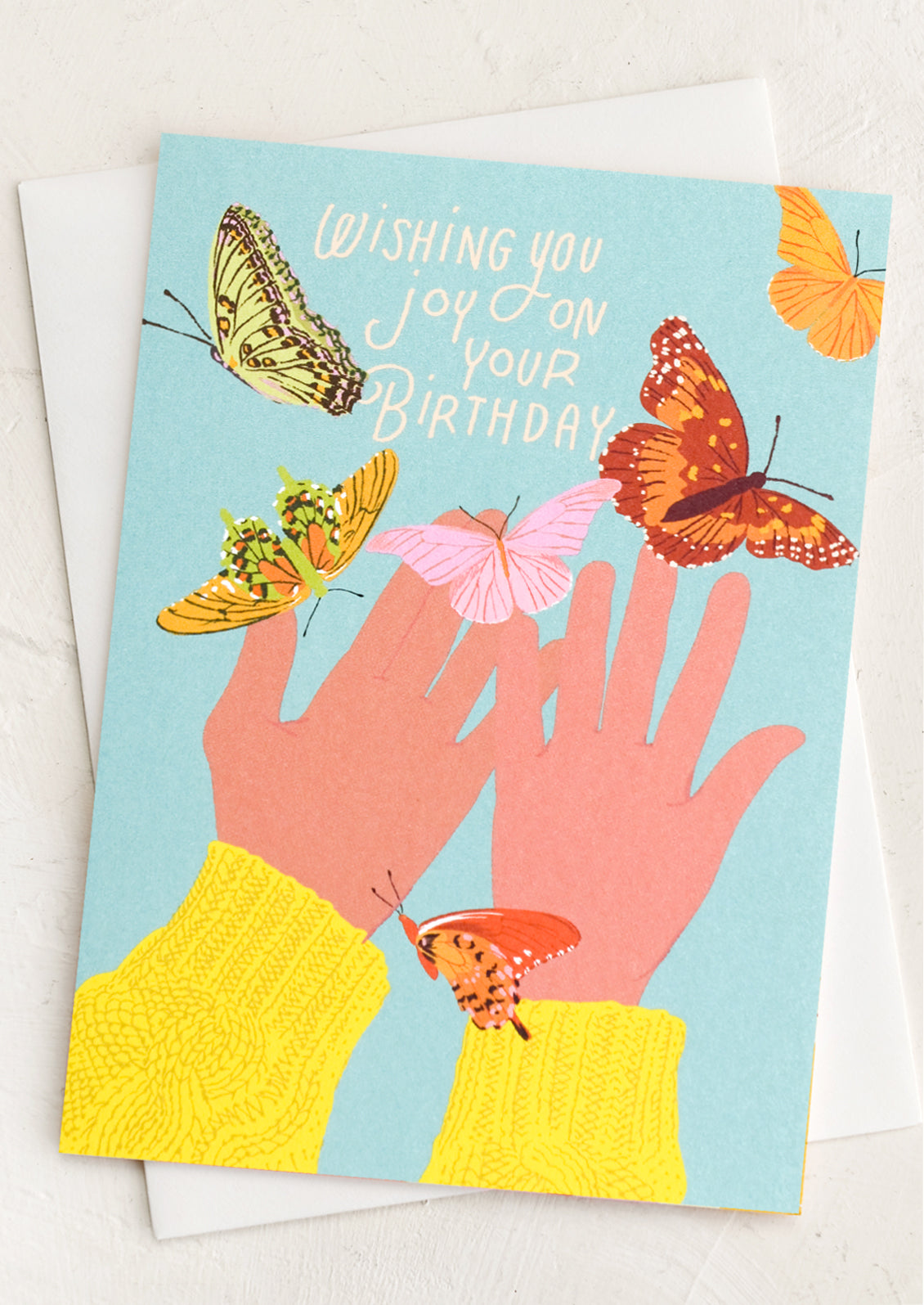 A card with illustration of butterflies on pair of human hands, text reads "Wishing you joy on your birthday".