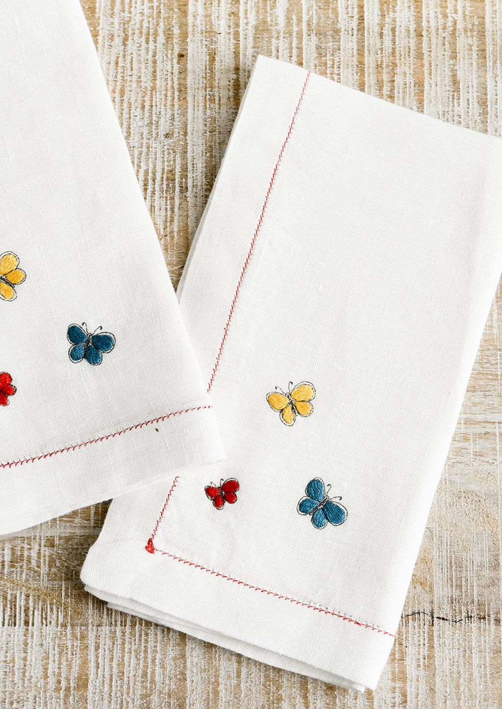 Primary Multi: White linen napkins with primary colored butterfly embroidery.