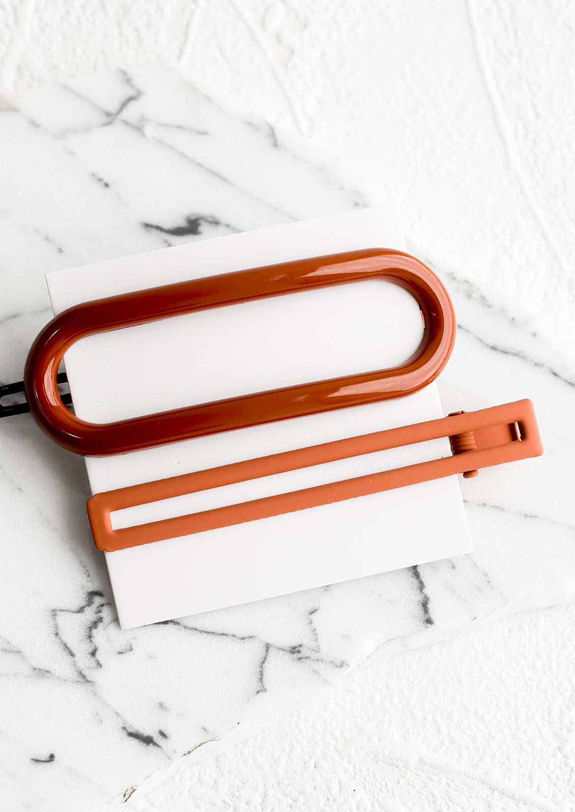 A pair of hair clips in oval and rectangular shapes in shades of rust.