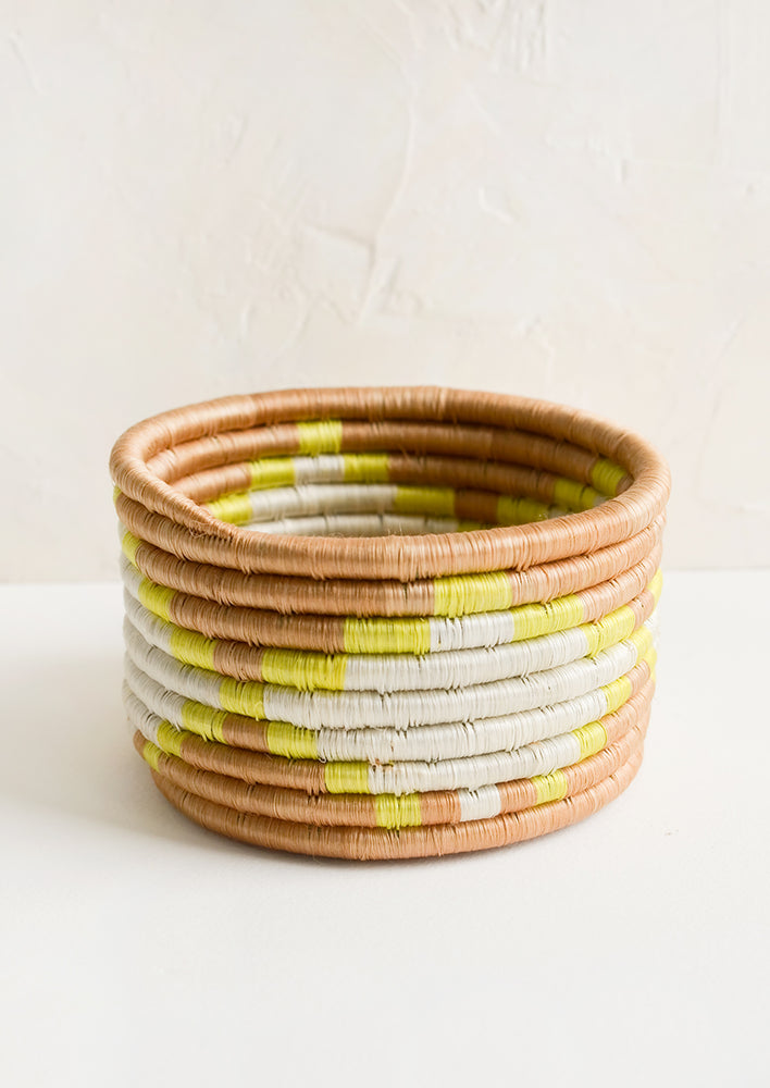 1: A round catchall basket in woven sweetgrass with yellow and white motif pattern.