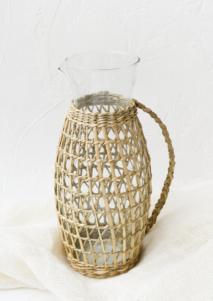 1: A tall, lean, clear glass pitcher with woven seagrass exterior