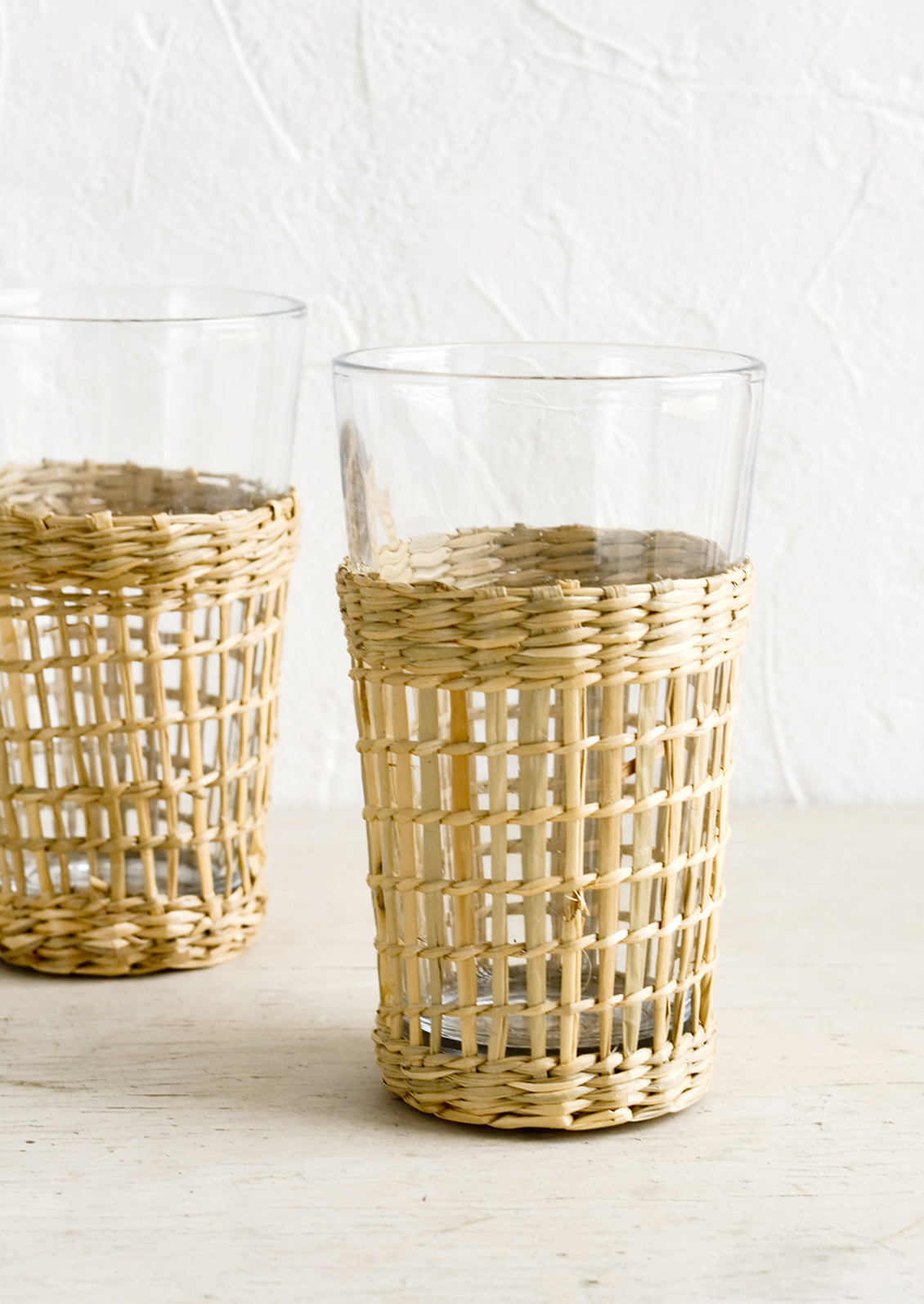 Tall glass cups wrapped in decorative seagrass cage.