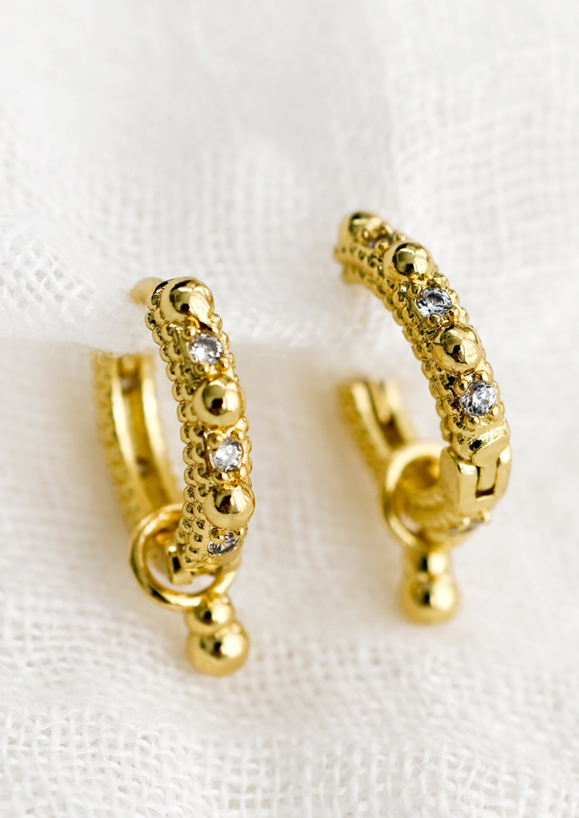 A pair of textured gold hoop earrings with crystal detailing.