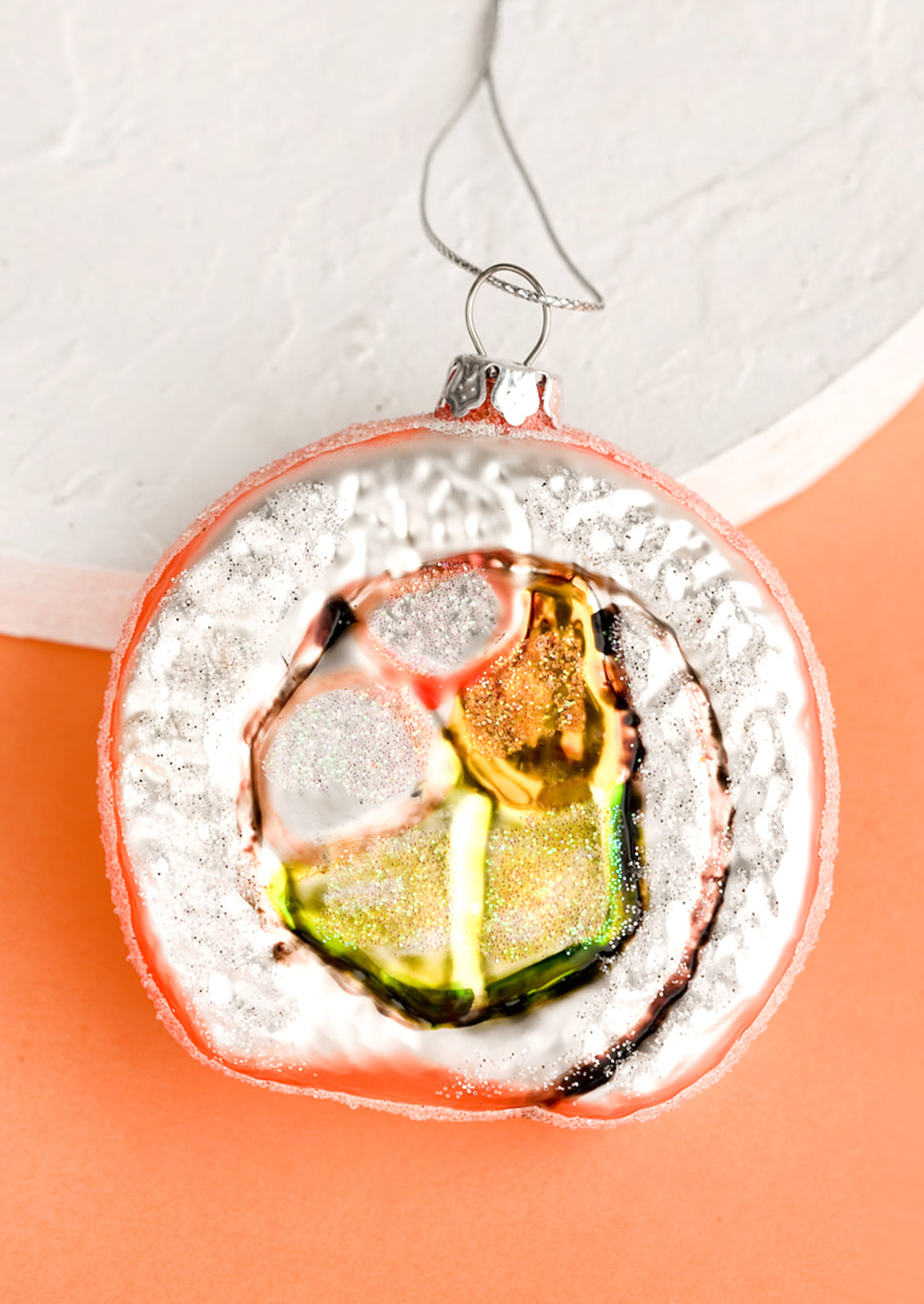 A glass holiday ornament of a california sushi roll slice.