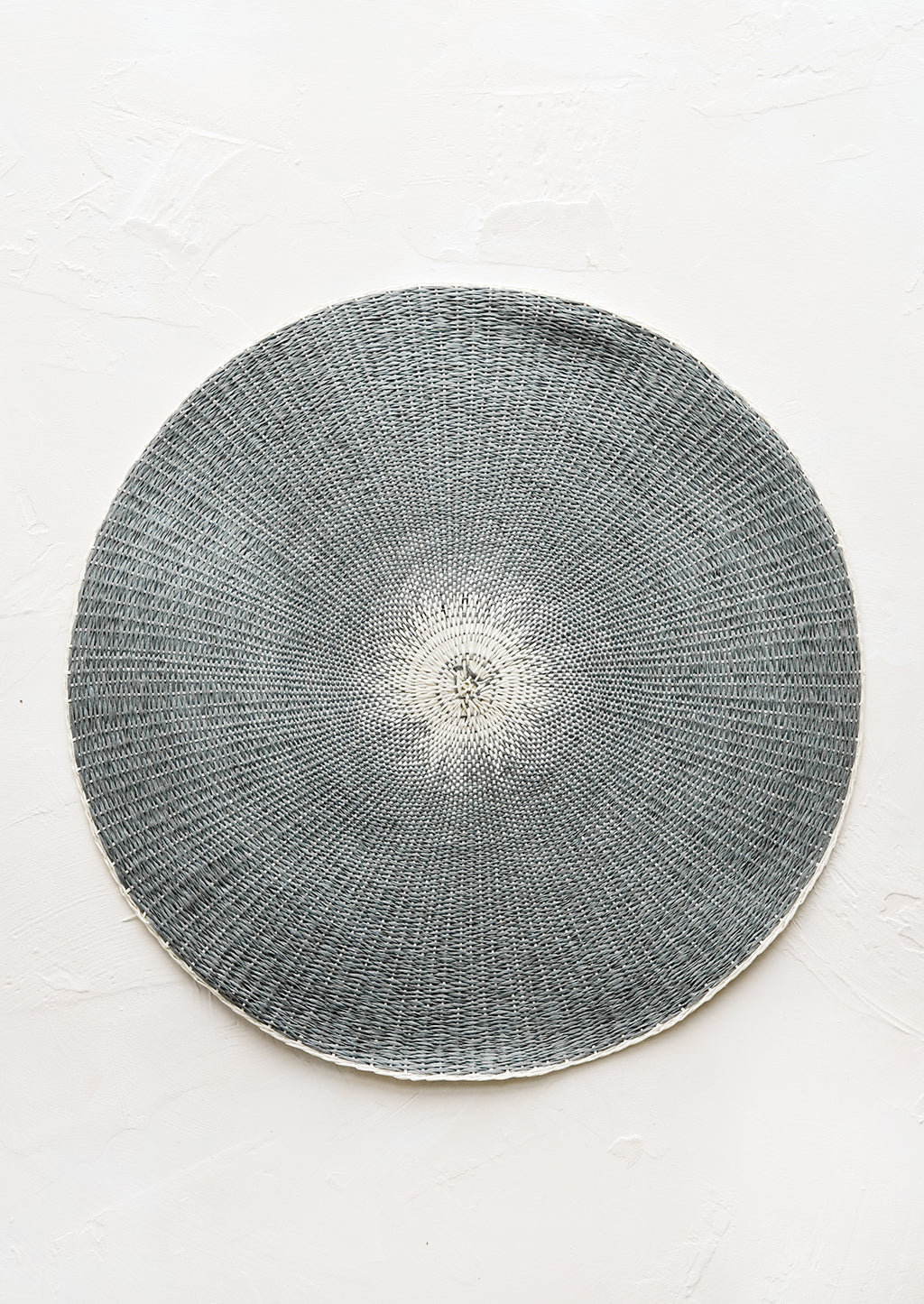 Dark Grey: A round straw placemat in dark grey with white spot at center.
