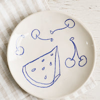 1: A ceramic side plate with still life fruit drawings in blue.