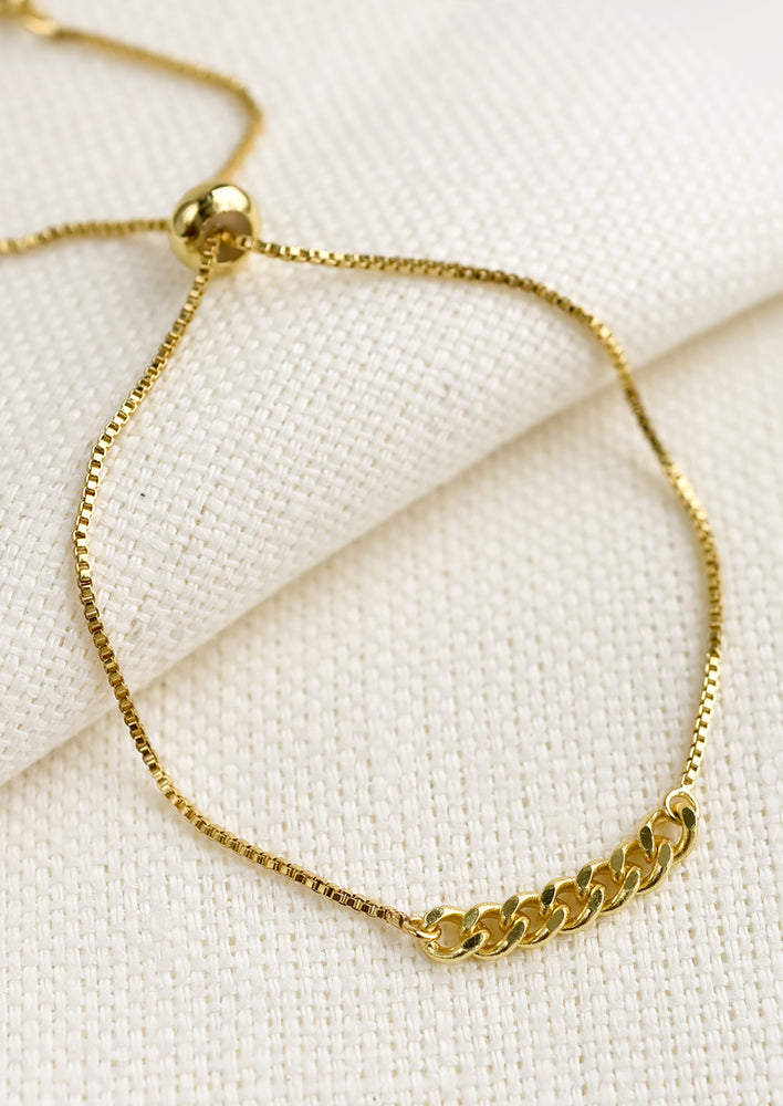 An adjustable gold bracelet with chainlink charm.