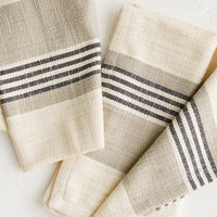 Tan / Black Stripe: A pair of folded napkins in ivory with black and tan striped band across middle.