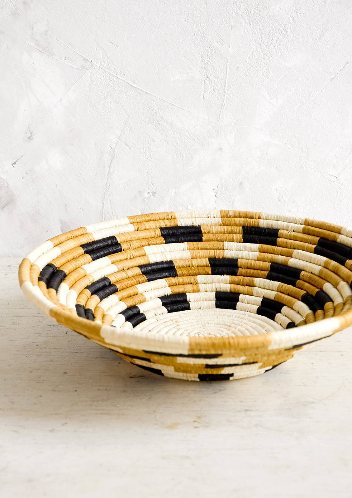 Round, shallow bowl made from woven raffia in checkered pattern and neutral palette