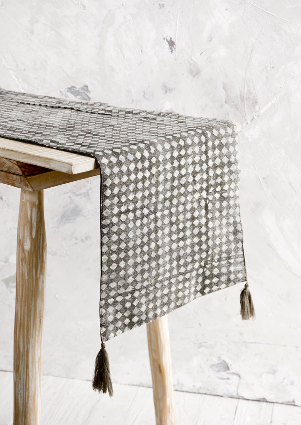 1: Table runner shown on a console table. Distressed grey with white stamped diamond print and tassels at corners.