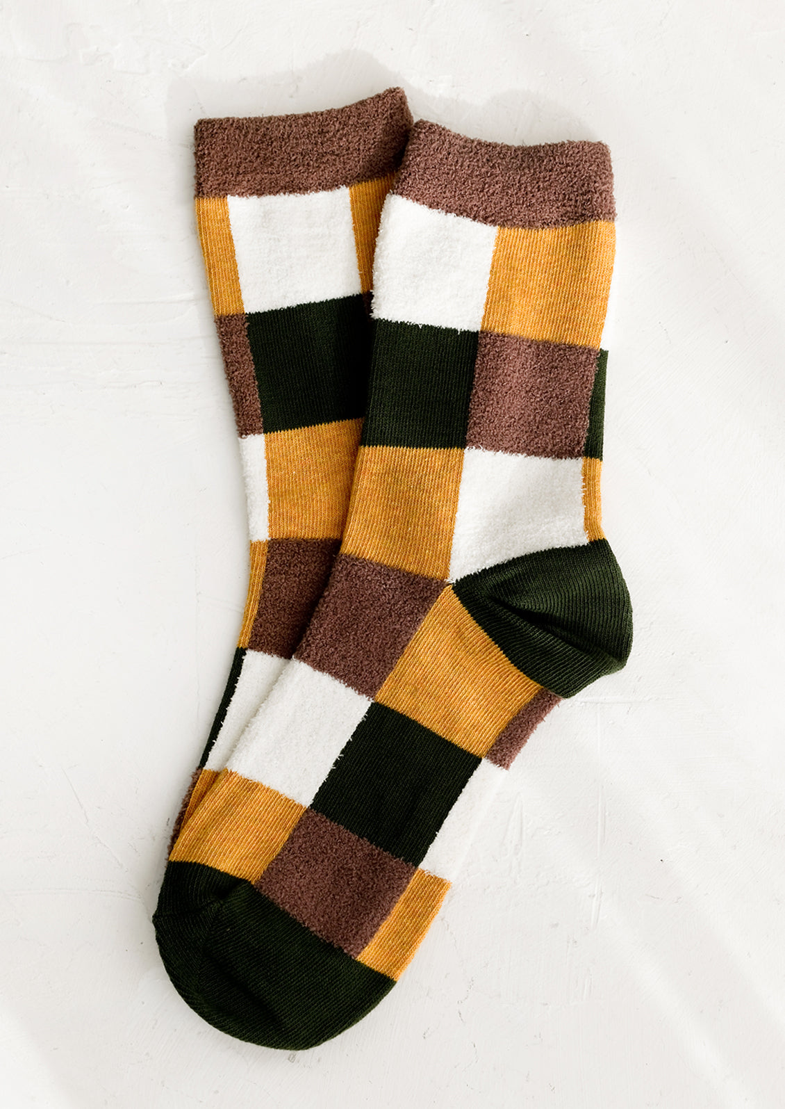 A pair of checkered socks in olive, mustard and white with fuzzy brown accents.