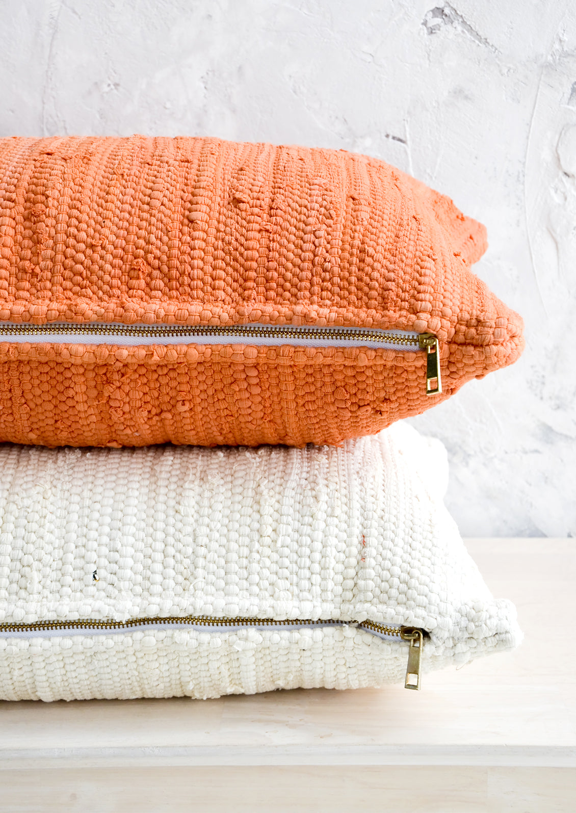 Two lumbar throw pillows on their sides, revealing exposed brass zip closures at bottom.