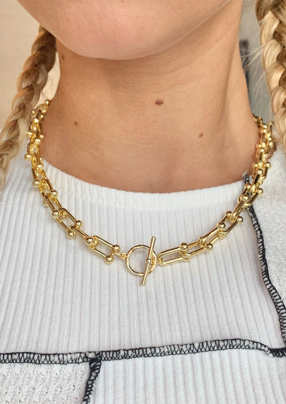 A woman wearing a gold chainlink necklace with toggle closure at front and center.