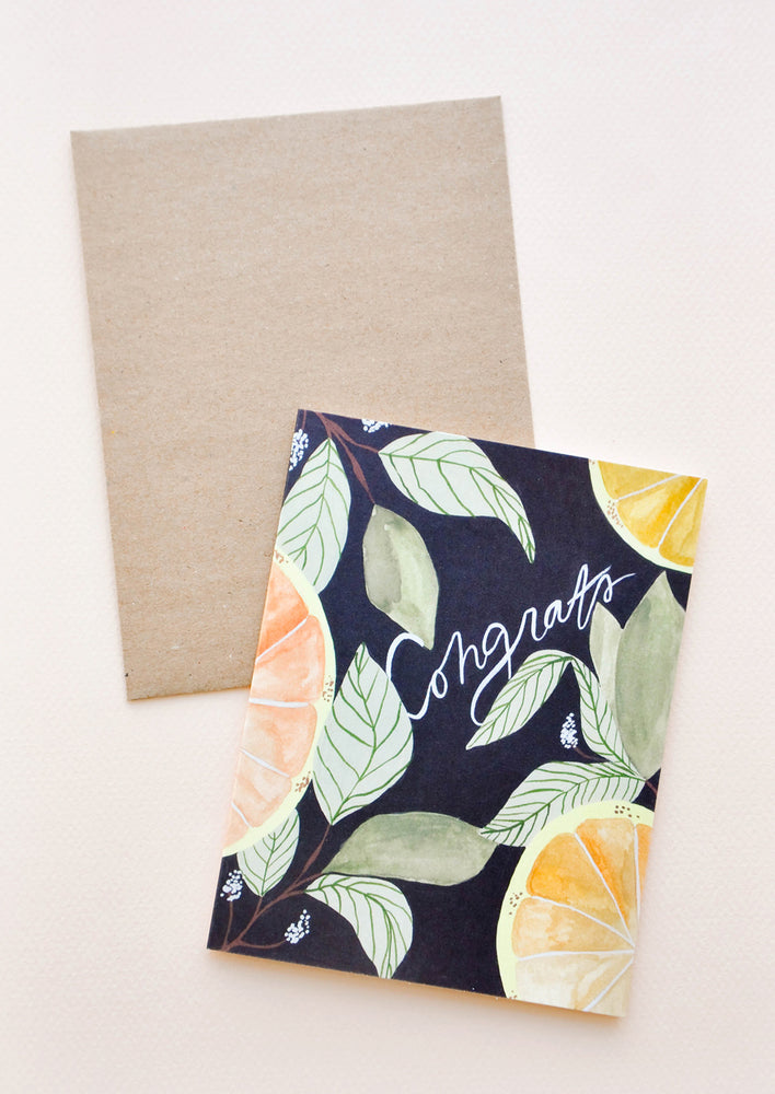 1: Notecard with citrus fruits and leaves on black ground and the text "Congrats", with brown envelope.