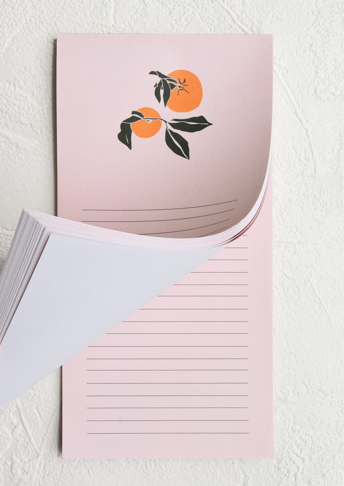 A light pink lined notepad with two oranges at the top
