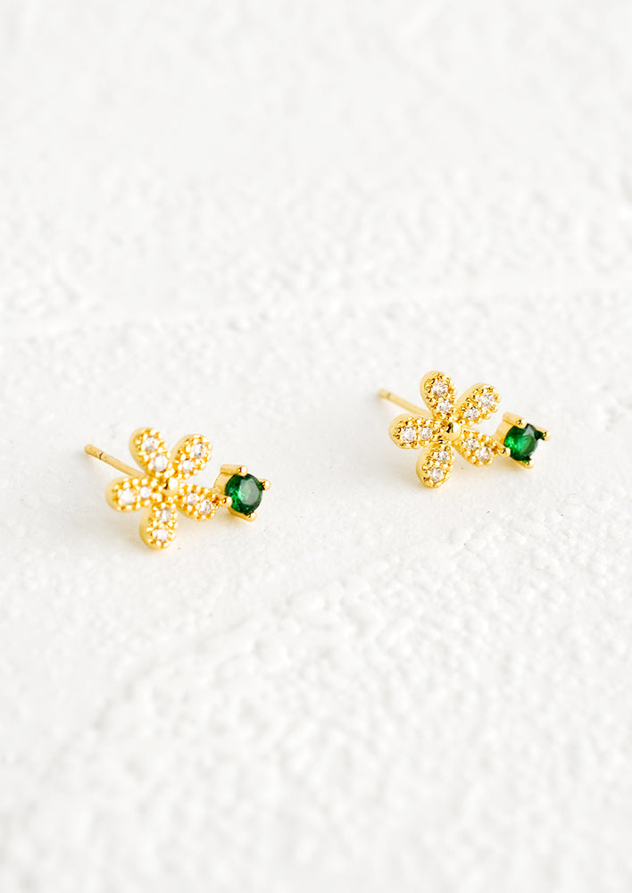 A pair of stud earrings with a gold and crystal flower shape attached to a round emerald colored stone.