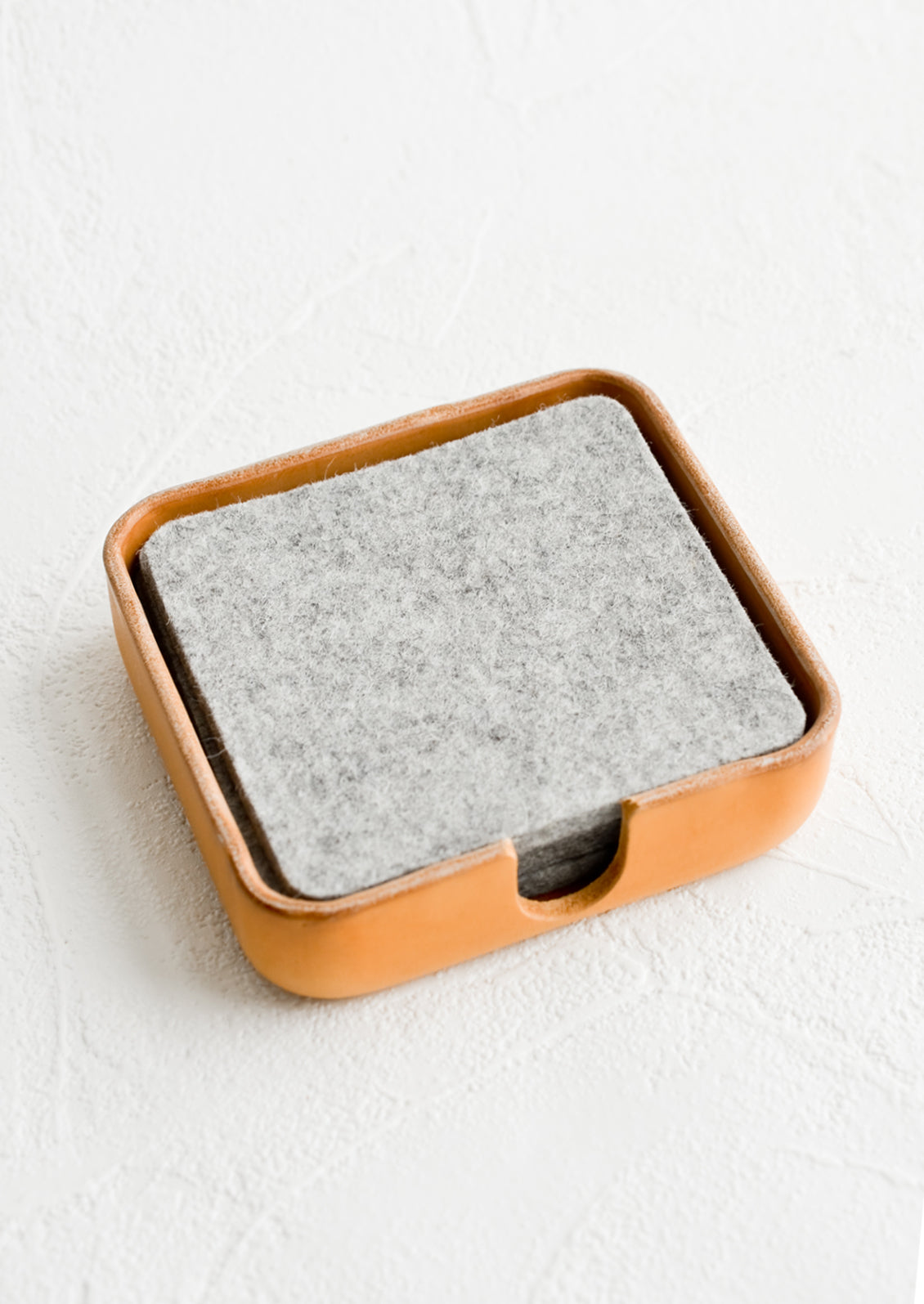 A leather coaster holder containing grey felt coasters.