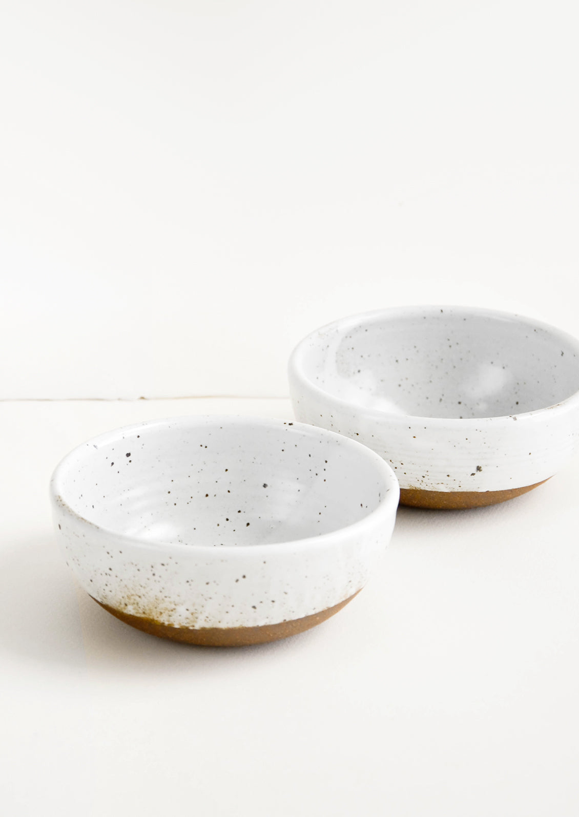 Two glossy white ceramic bowls with brown speckles.