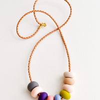 Indian Summer: Woven leather cord necklace with gold clasp and rounded clay beads tans, pinks, purple, blue, gray, and chartreuse.