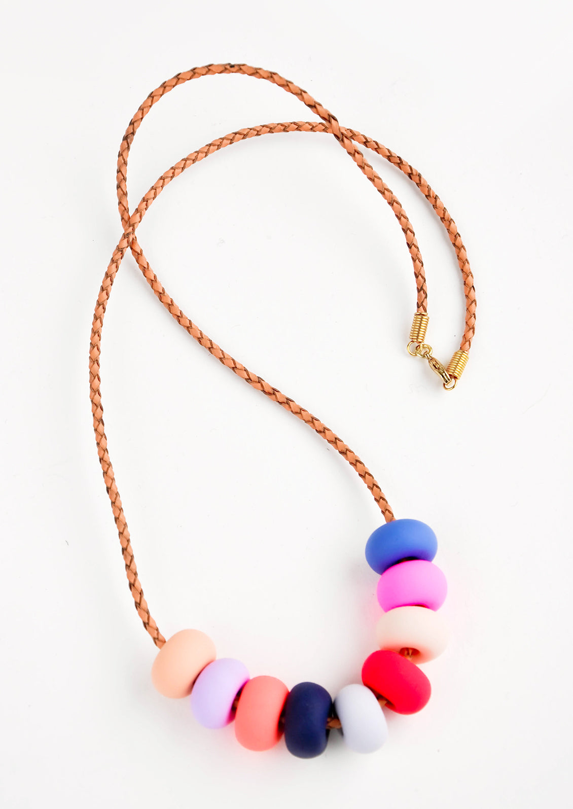 Woven leather cord necklace with gold clasp and rounded clay beads pinks, reds, blues, and purple.