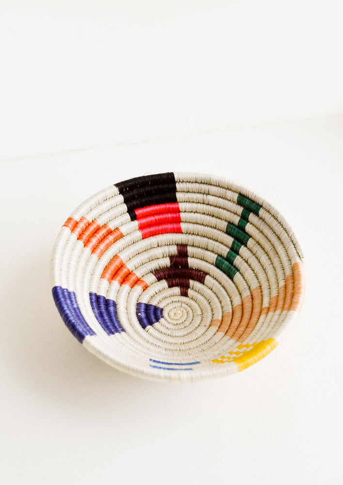 Shallow bowl made of woven fiber in a mix of bright colors and geometric shapes