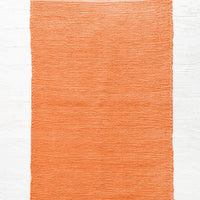Paprika: Cotton flatweave rug in solid color red orange with slight texture, fringe trim on two ends