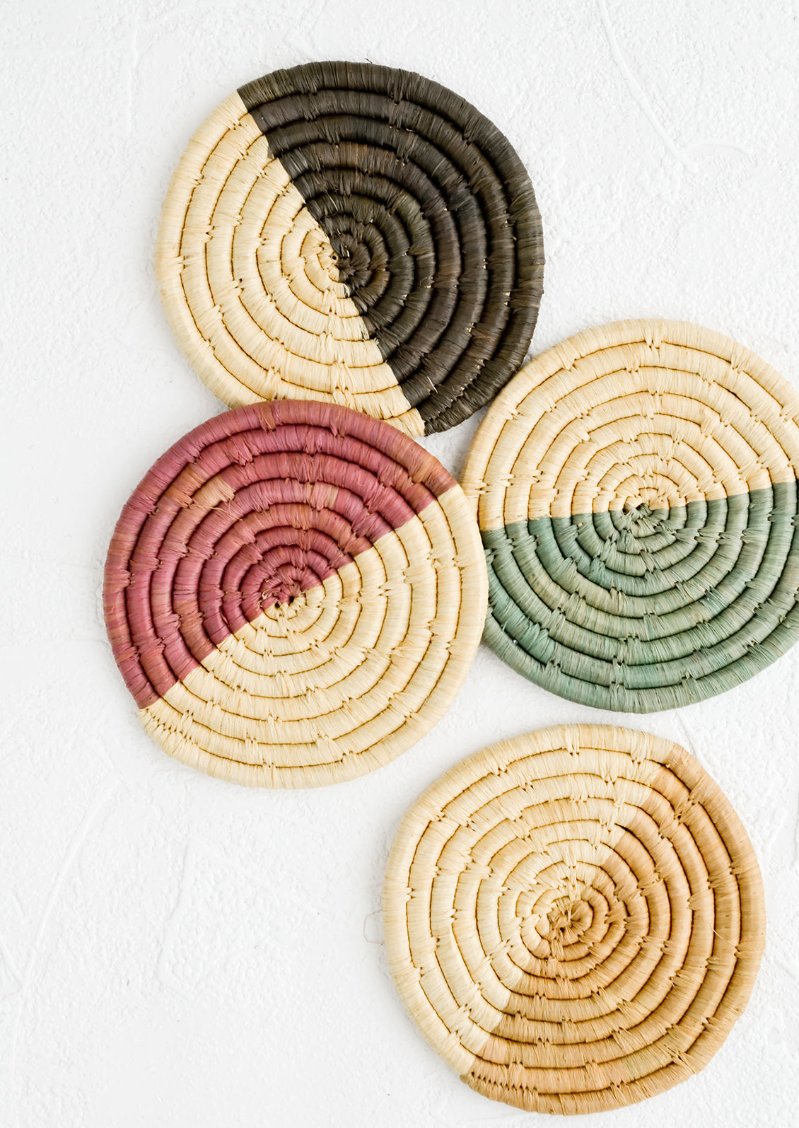 A set of four coasters in color blocked raffia, each a different color.