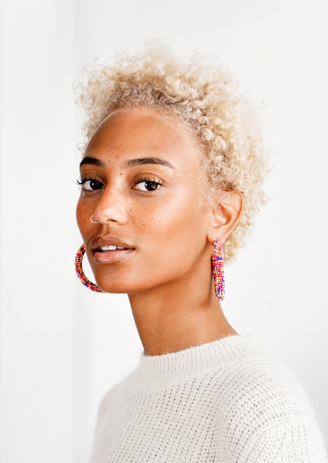 Model wears multicolored beaded hoop earrings and white sweater.