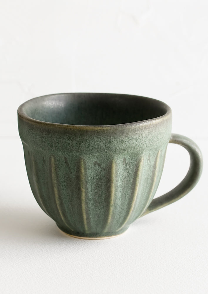 A ceramic mug with grooved texture in rustic dark green glaze.