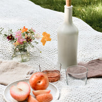 Tall / Satin White: An outdoor picnic setting with wine and pluots.