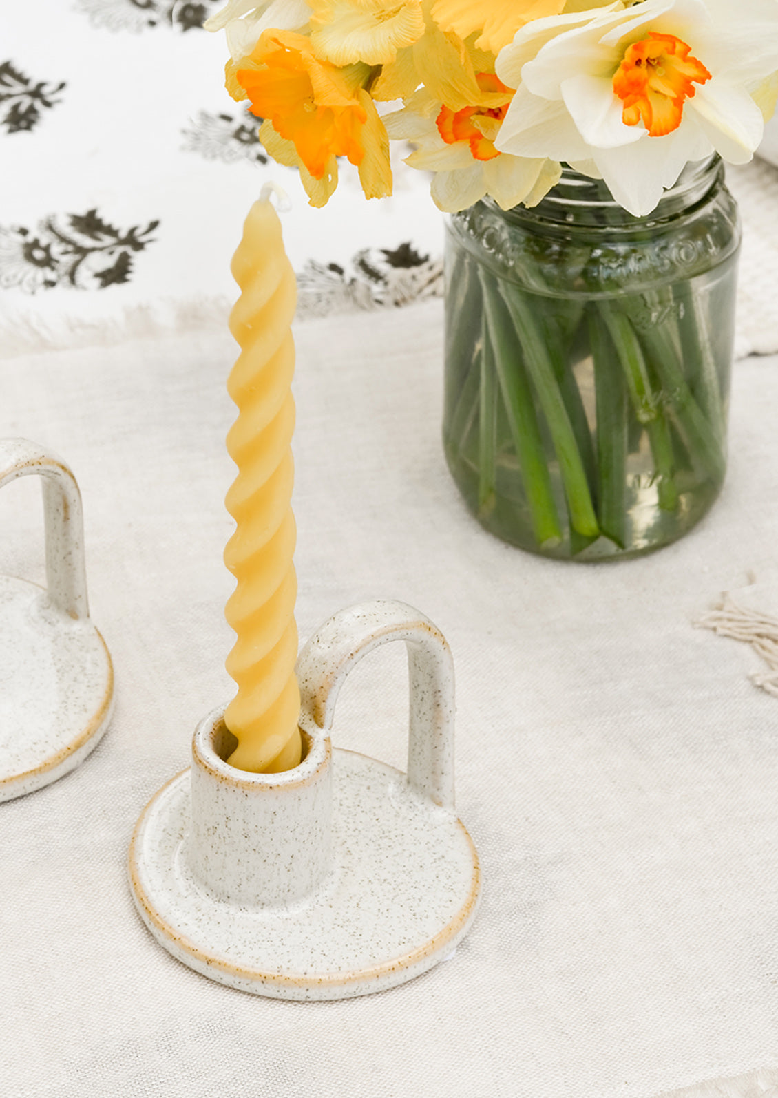 A spiral beeswax taper candle in a ceramic holder on table setting.