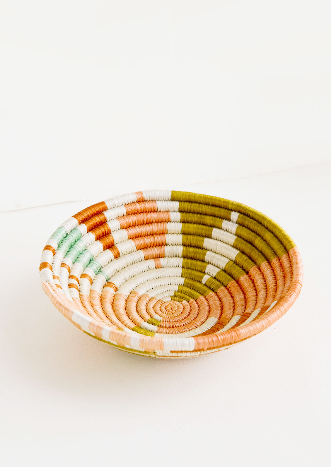 Shallow bowl made of woven fiber in a mix of pastel colors and geometric patterns