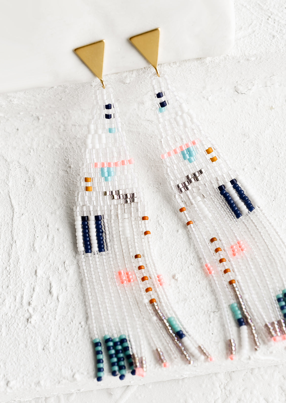 A pair of beaded statement earrings with triangular post and fringed shape in clear beads.