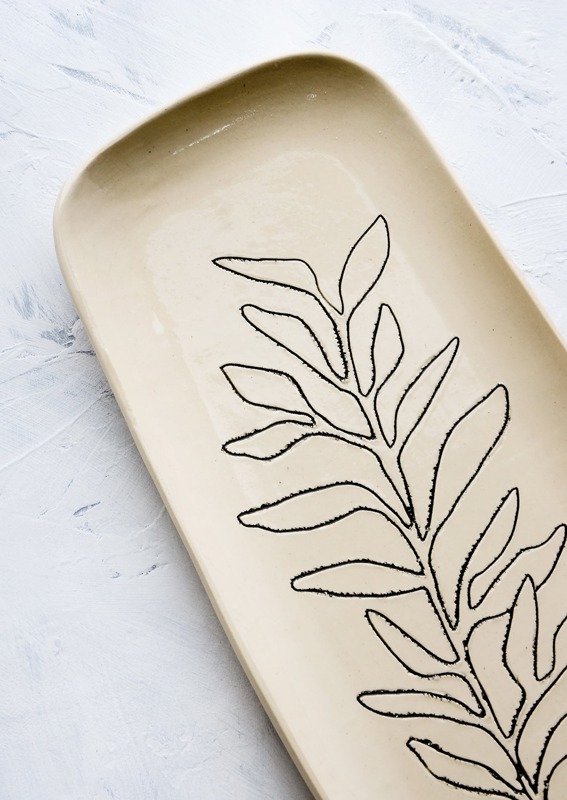 Black etched botanical detailing on a ceramic platter.