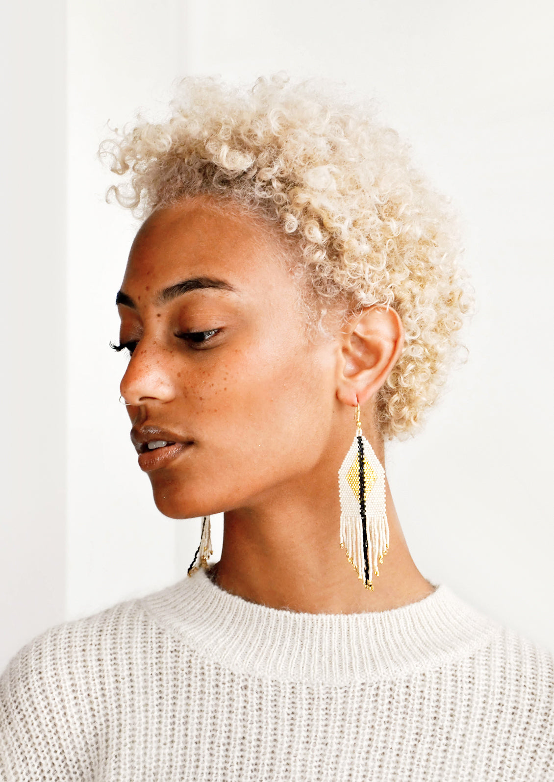 Model wears ivory fringe earrings with black stripe down the center.