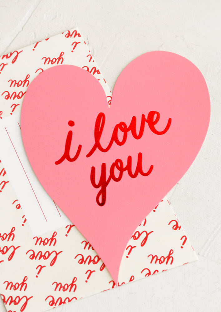 A heart shaped pink card with "I love you" in red letters.