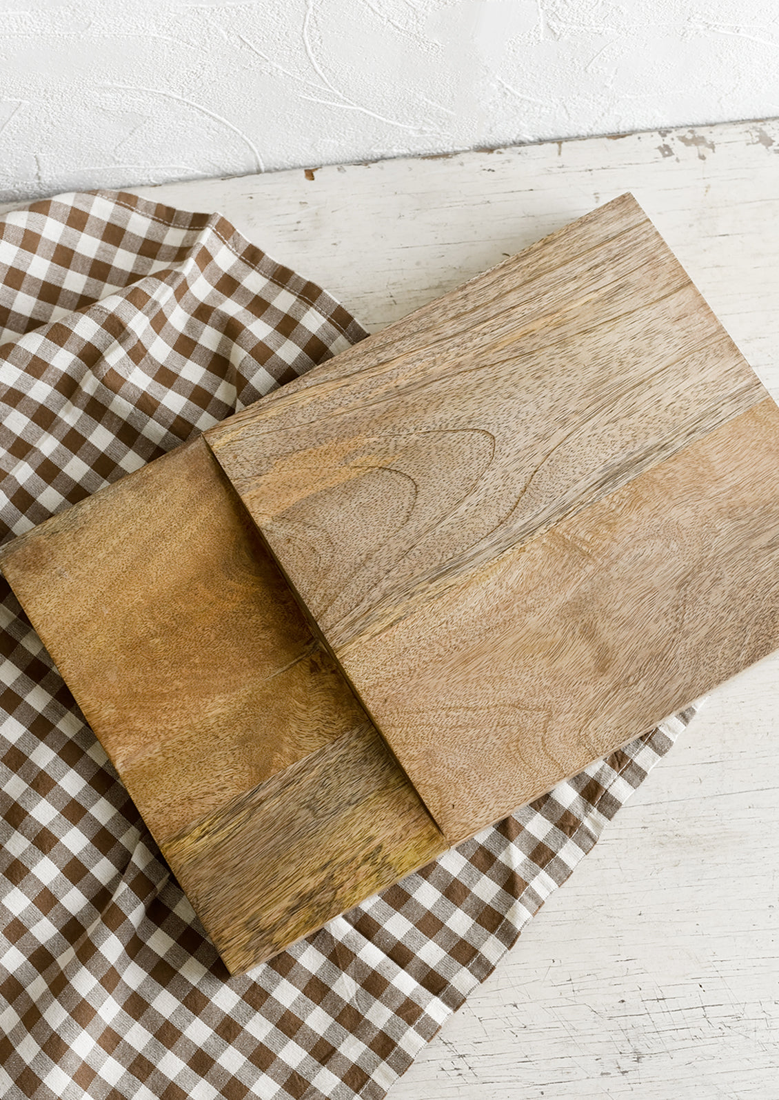 A mango wood cutting board resting on a gingham tea towel.