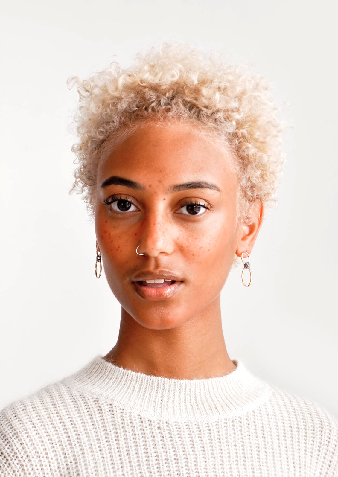 Model wears gold hoop earrings and cream colored sweater.