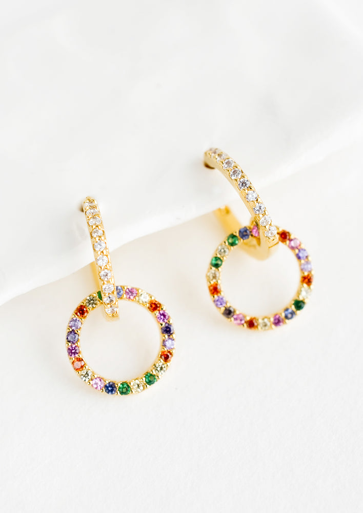 A pair of huggie earrings in double hoop design, one with clear crystals and one with multicolor crystals.