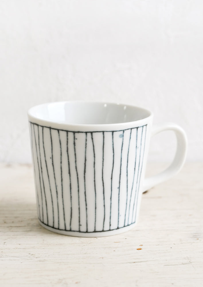 A glossy white ceramic mug with hand-drawn line pattern in dark indigo.